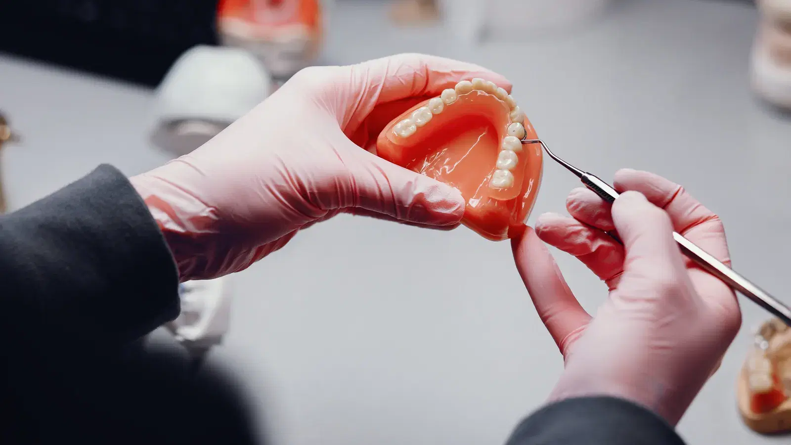 Gloved hands holding a denture and checking a tooth with a fine dental instrument