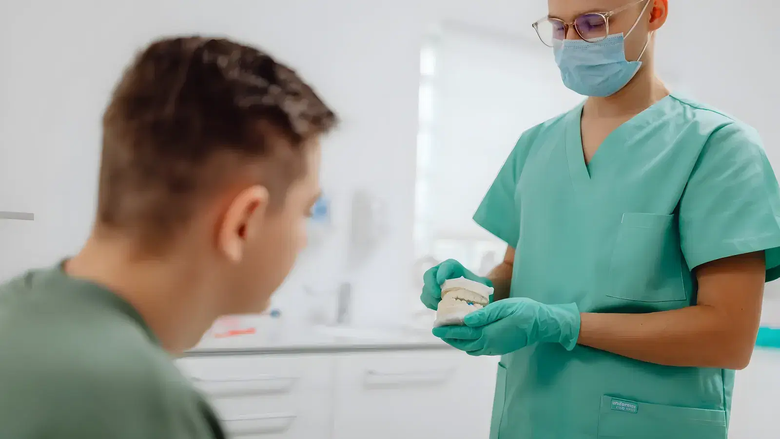 A dentist holding a model of the teeth, talking a seated patient through the treatment being recommended