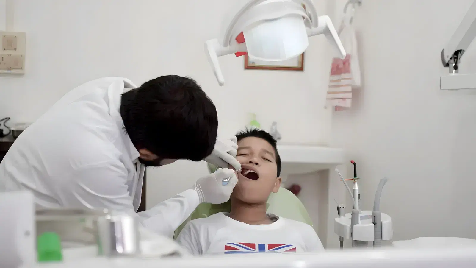 A young boy lying back in the dental chair with his mouth open while a dentist leans in to check his teeth
